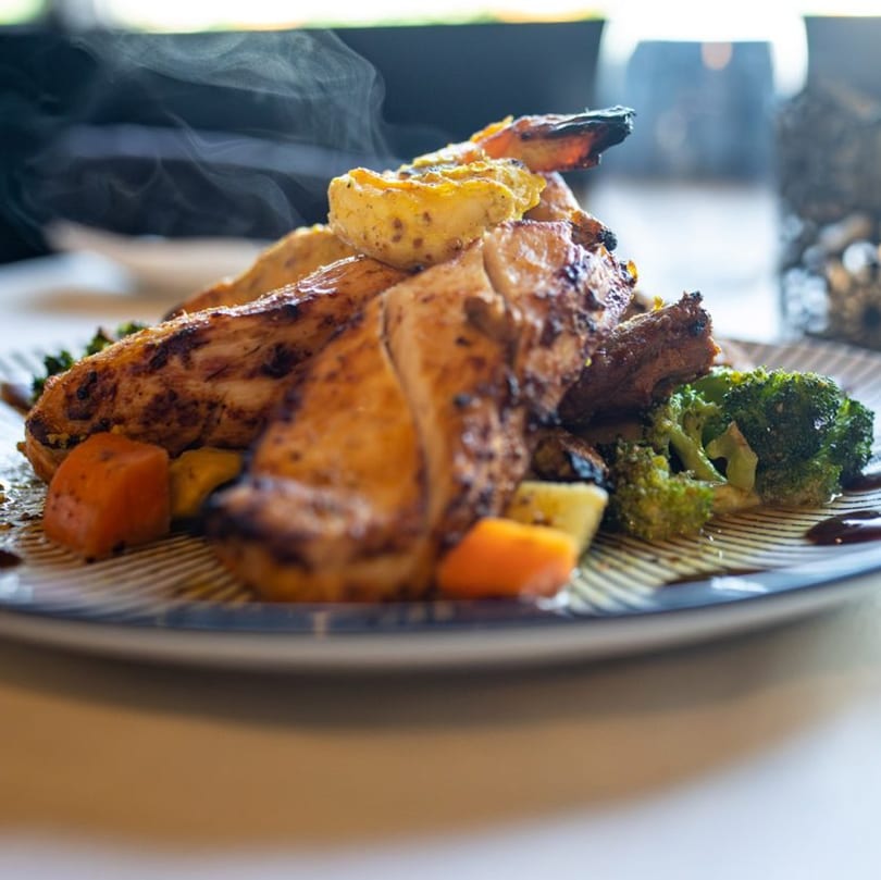 Steaming grilled chicken with broccoli and carrots on a striped plate at Bazil Indian Cuisine.