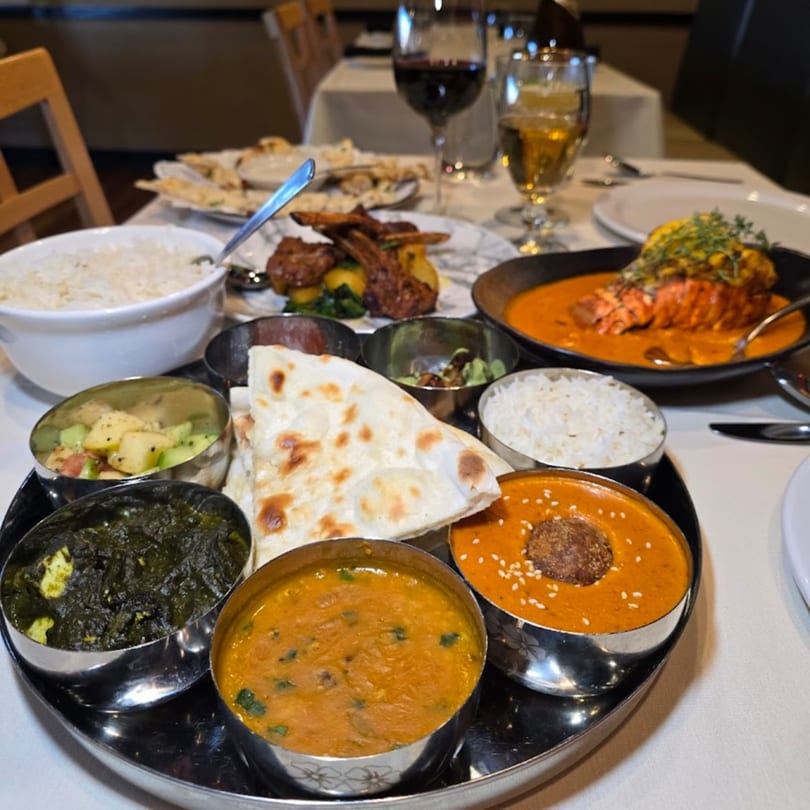 A Bazil Indian Cuisine thali with various dishes, naan, rice, and a lobster entree.