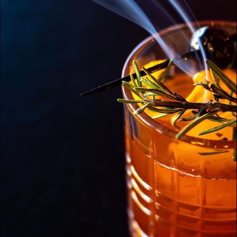 Smoky cocktail with rosemary and orange peel in a textured glass at Bazil Indian Cuisine.